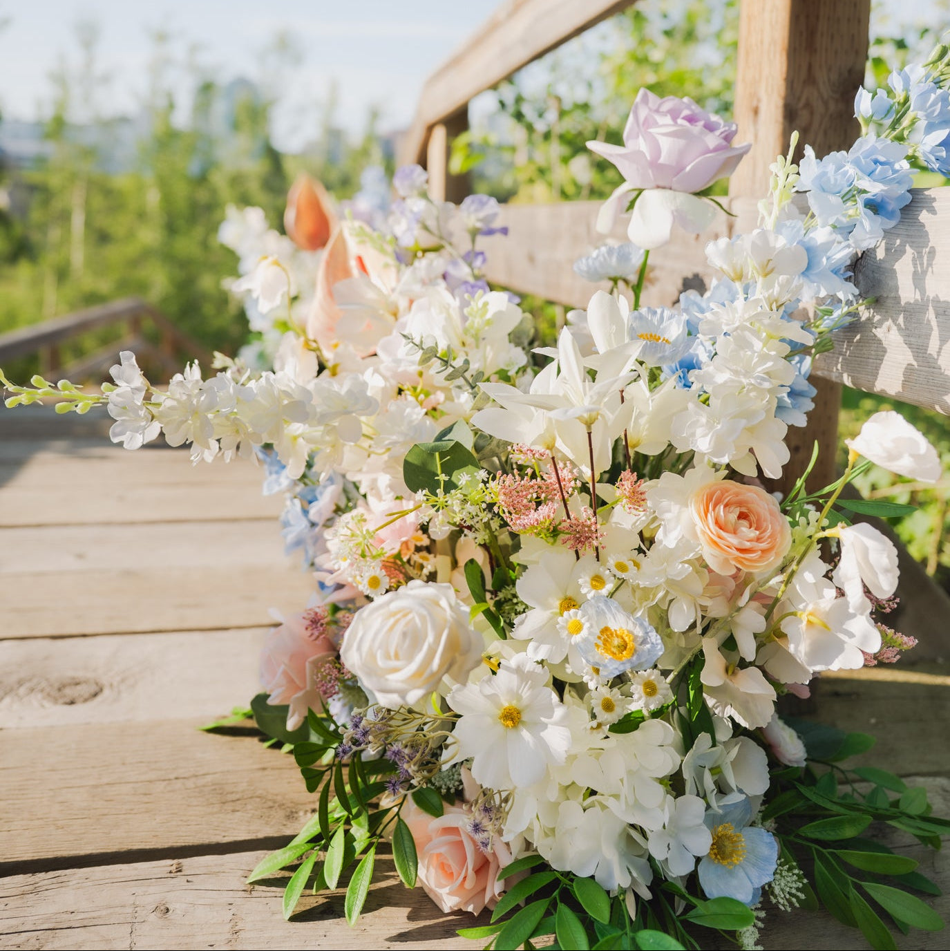 Pastel faux flower floor arrangement with roses, hydrangeas, and orchids styled against a wooden bridge, ideal for Edmonton weddings as aisle or sweetheart table decor.