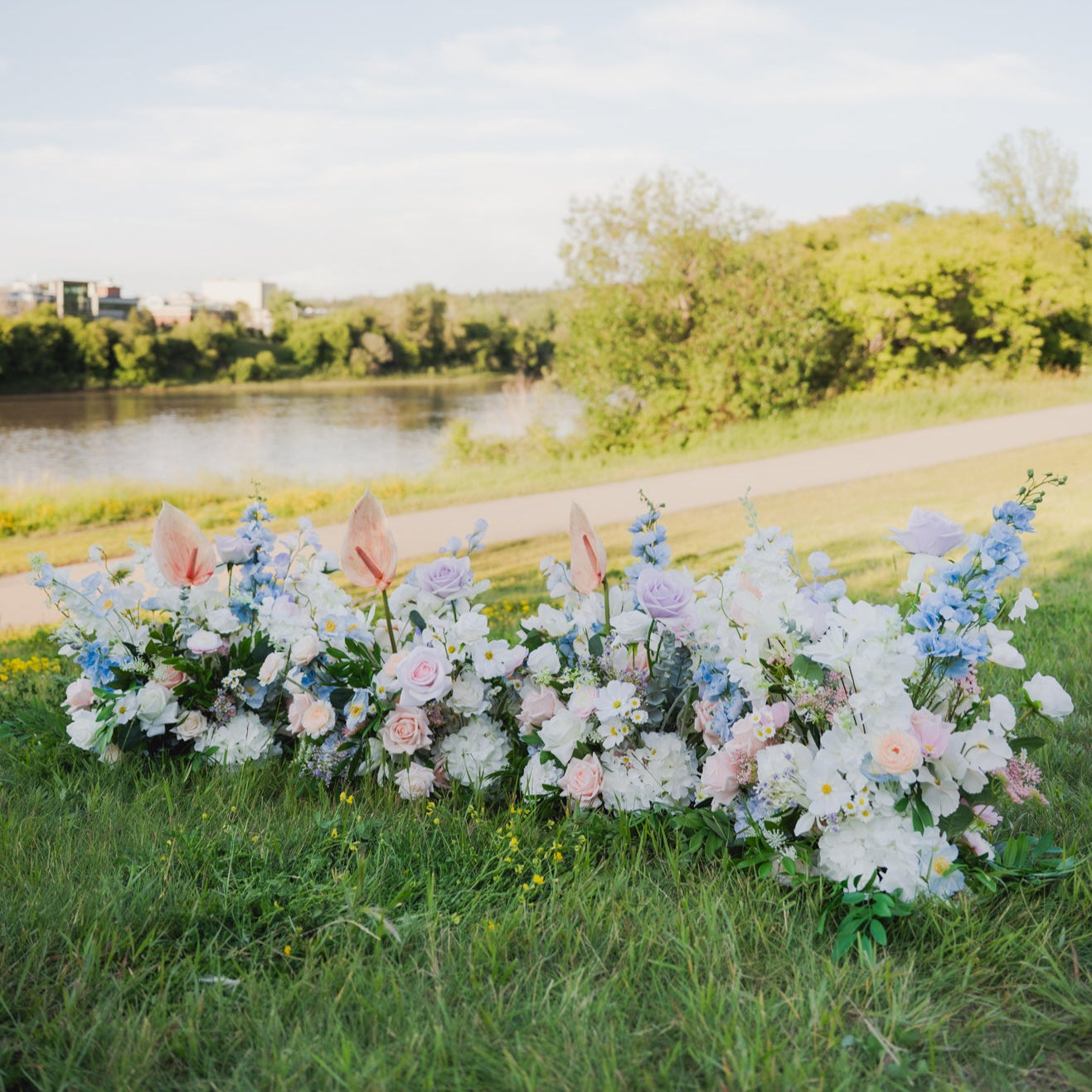 Pastel Petal faux floor floral arrangements in blush, lilac, blue, and ivory set on grass outdoors, perfect for Edmonton wedding aisle decor or ceremony backdrop rentals.