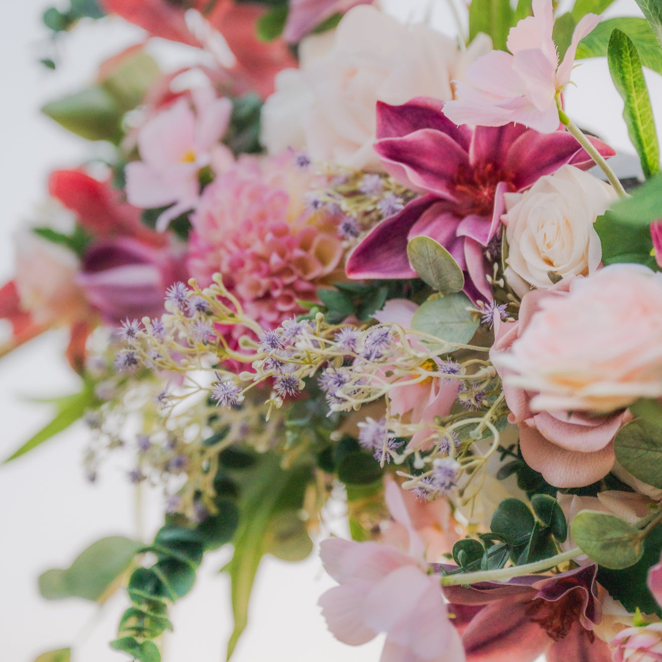 Plum Bliss arch floral arrangement of pink, purple, and green flowers with green leaves on a white background