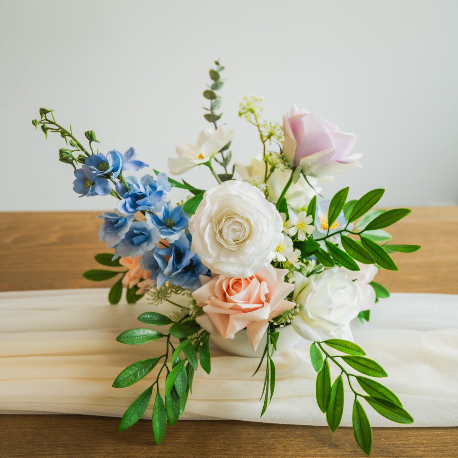 Artificial pastel wedding centerpiece with faux roses, white ranunculus, and blue delphinium in Edmonton for receptions and special events.