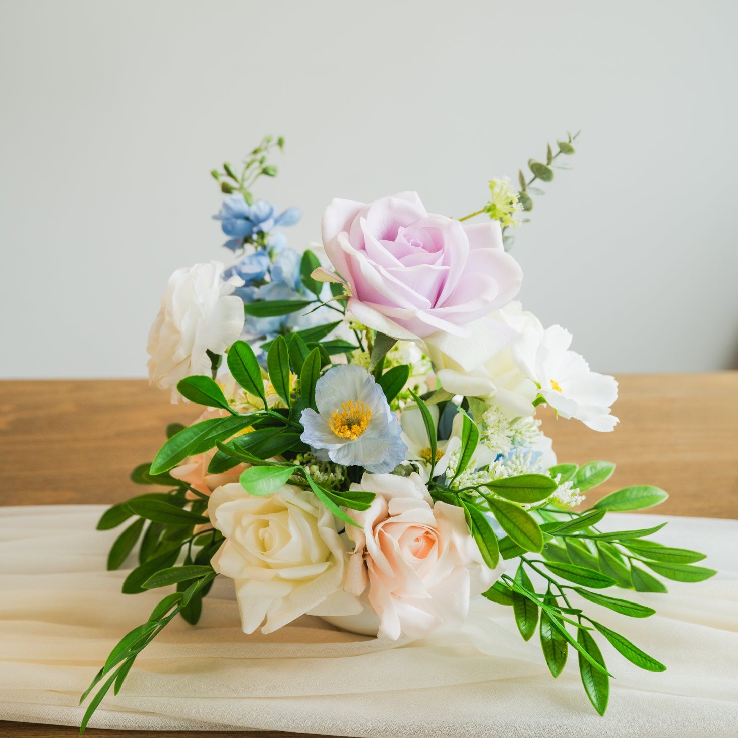 Faux pastel floral centerpiece with pink roses, blue accents, and greenery, perfect for Edmonton weddings and event rentals.