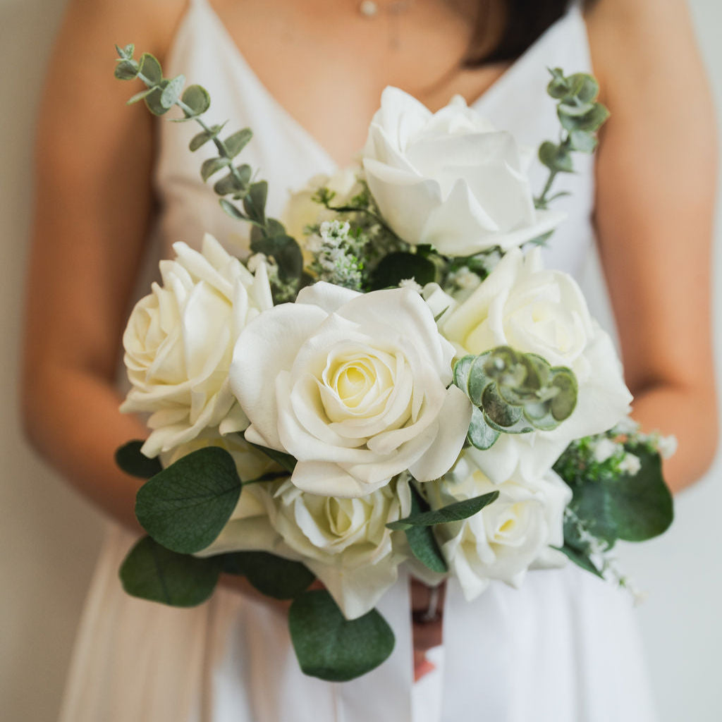 Bridal bouquet of real touch (artificial) white roses held by a person wearing a white dress for her wedding.