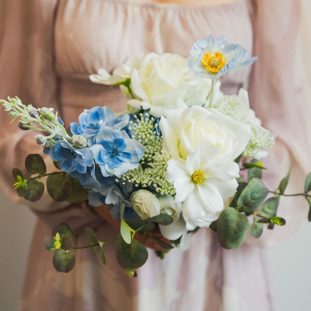 Bouquet of faux (artificial, real touch and silk) flowers held by a person wearing a light pink dress.