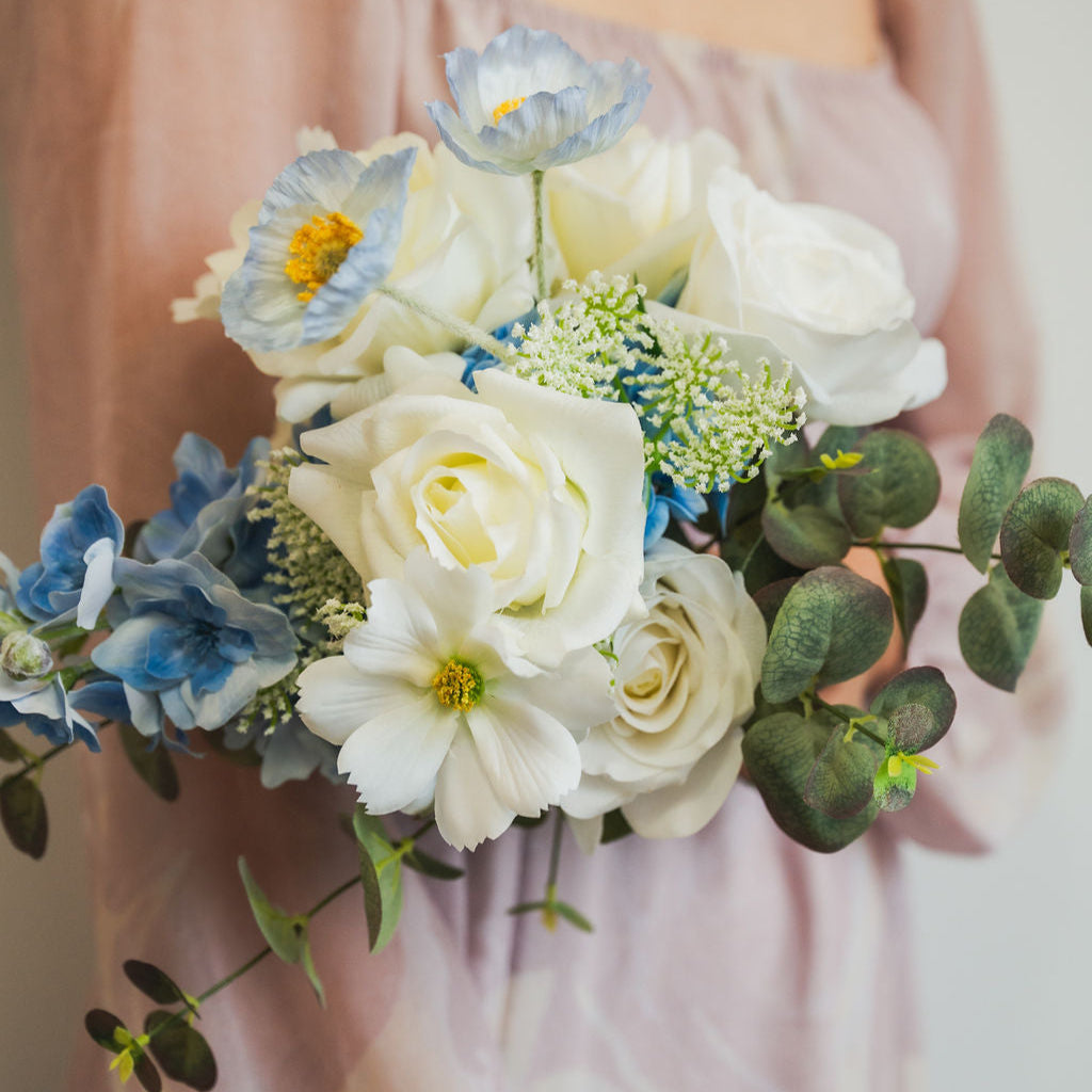 Bouquet of faux flowers held by a person wearing a light-colored dress.