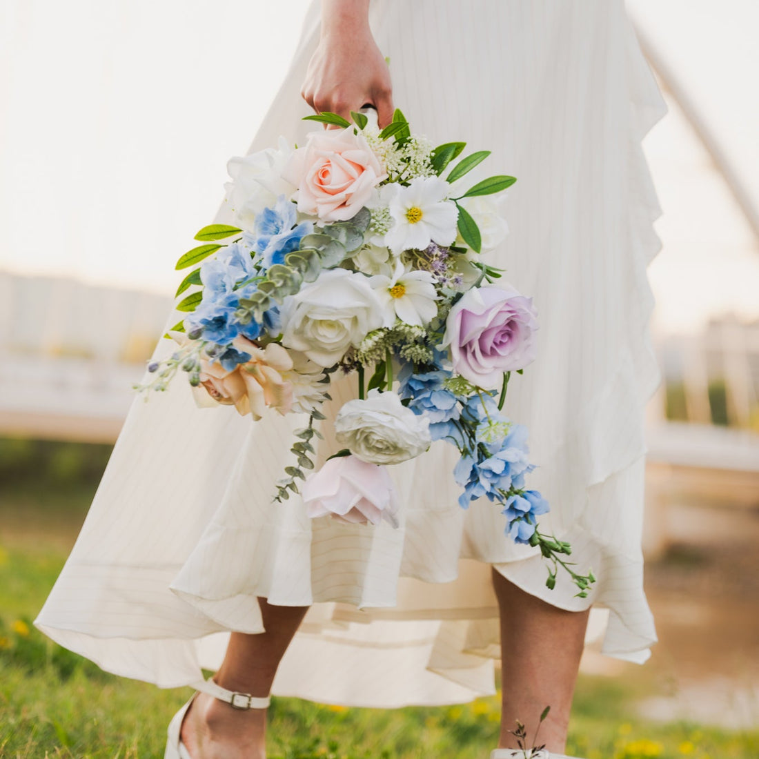 Person in a white dress holding a real touch, faux flower bouquet in a grassy field (Edmonton, AB).