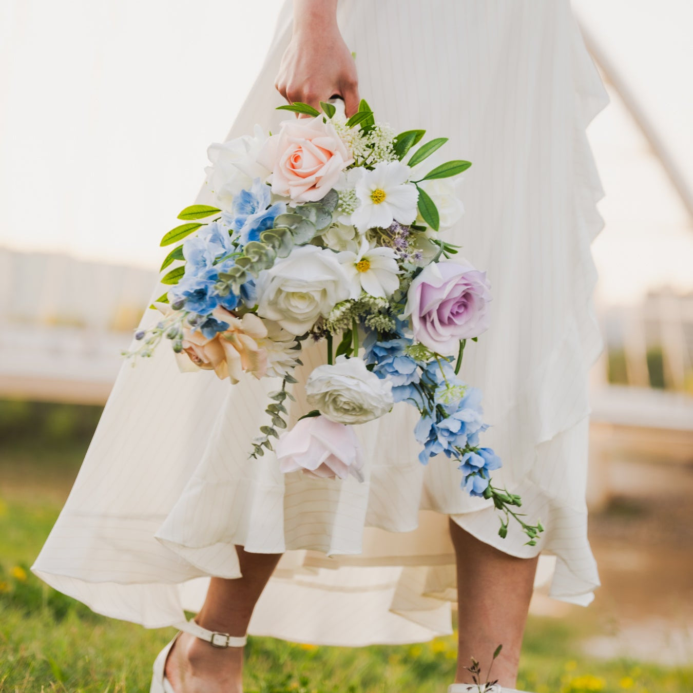 Person in a white dress holding a real touch, faux flower bouquet in a grassy field (Edmonton, AB).