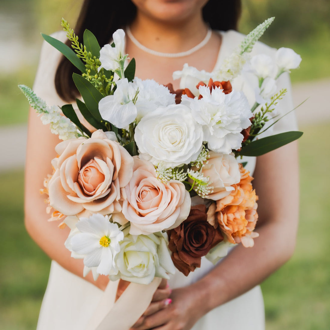 Bride in a white dress holding a Cocoa Bloom faux flower bouquet of silk roses and ranunculus in warm earthy tones.