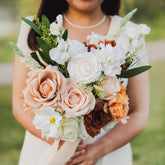 Bride in a white dress holding a Cocoa Bloom faux flower bouquet of silk roses and ranunculus in warm earthy tones.