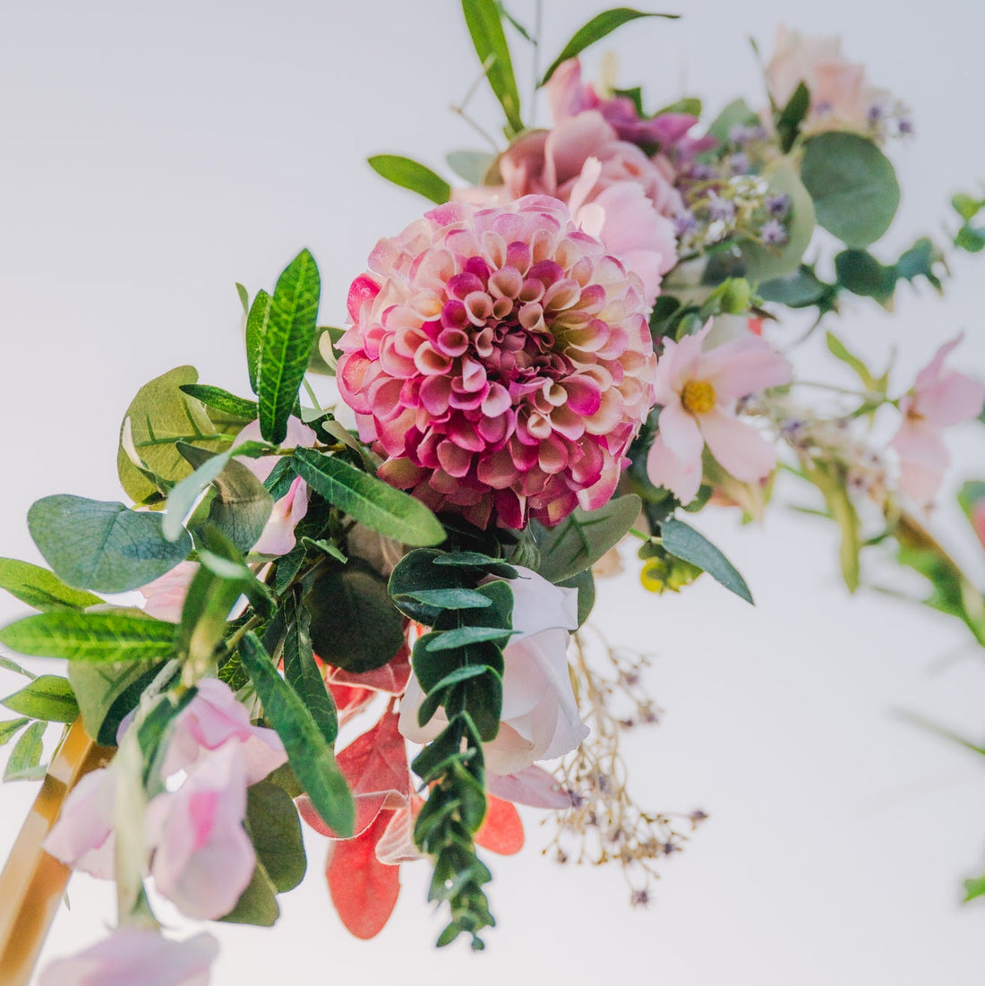 Arch floral arrangement with pink flowers and green leaves on a light background