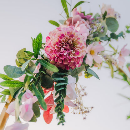 Arch floral arrangement with pink flowers and green leaves on a light background