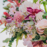 Plum Bliss arch floral arrangement of pink, purple, and green flowers with green leaves on a white background