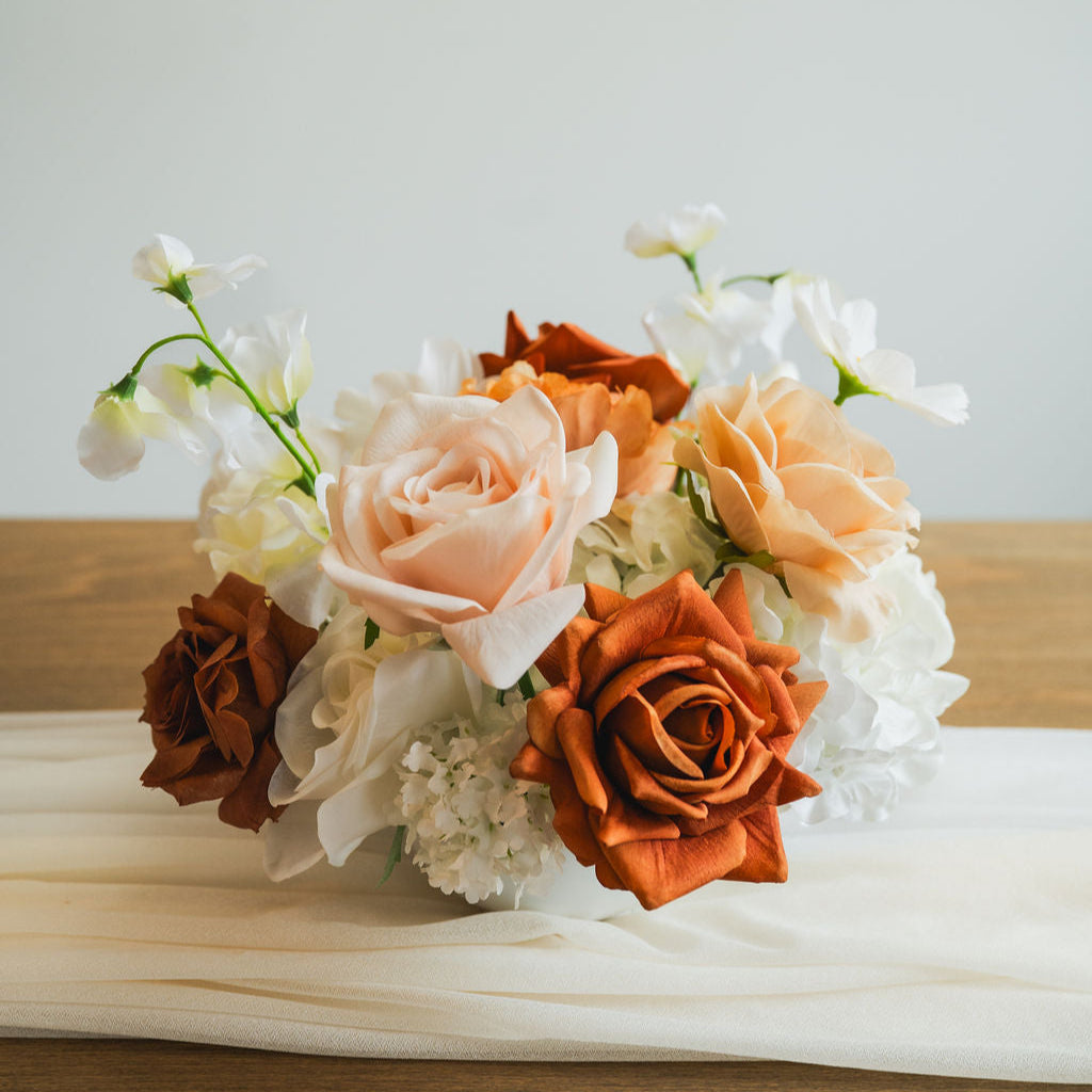 Close-up of Cocoa Bloom artificial floral arrangement with caramel, ivory, and copper roses, set in a white bowl vase on a neutral table runner.