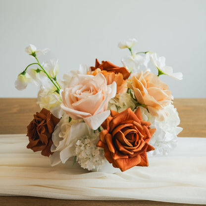 Close-up of Cocoa Bloom artificial floral arrangement with caramel, ivory, and copper roses, set in a white bowl vase on a neutral table runner.