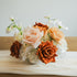 Close-up of Cocoa Bloom artificial floral arrangement with caramel, ivory, and copper roses, set in a white bowl vase on a neutral table runner.