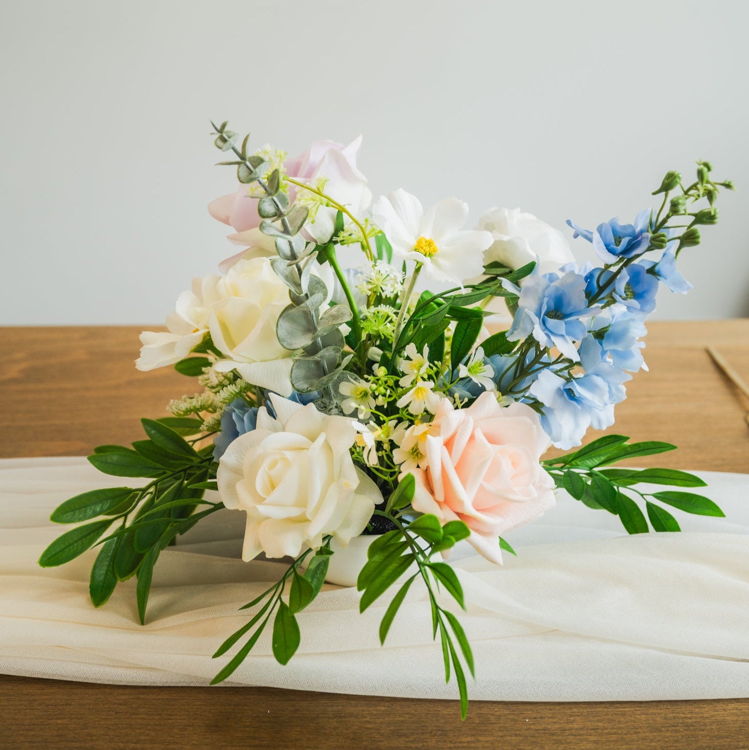 Artificial flower centerpiece with blush and ivory roses, blue faux blooms, and lush greenery, available for Edmonton wedding rentals.