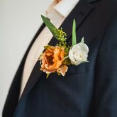 Side view of the Cocoa Bloom Groomsmen’s Boutonniere on a groomsmens navy suit, highlighting the warm cocoa flower, white rose, and leafy greens.