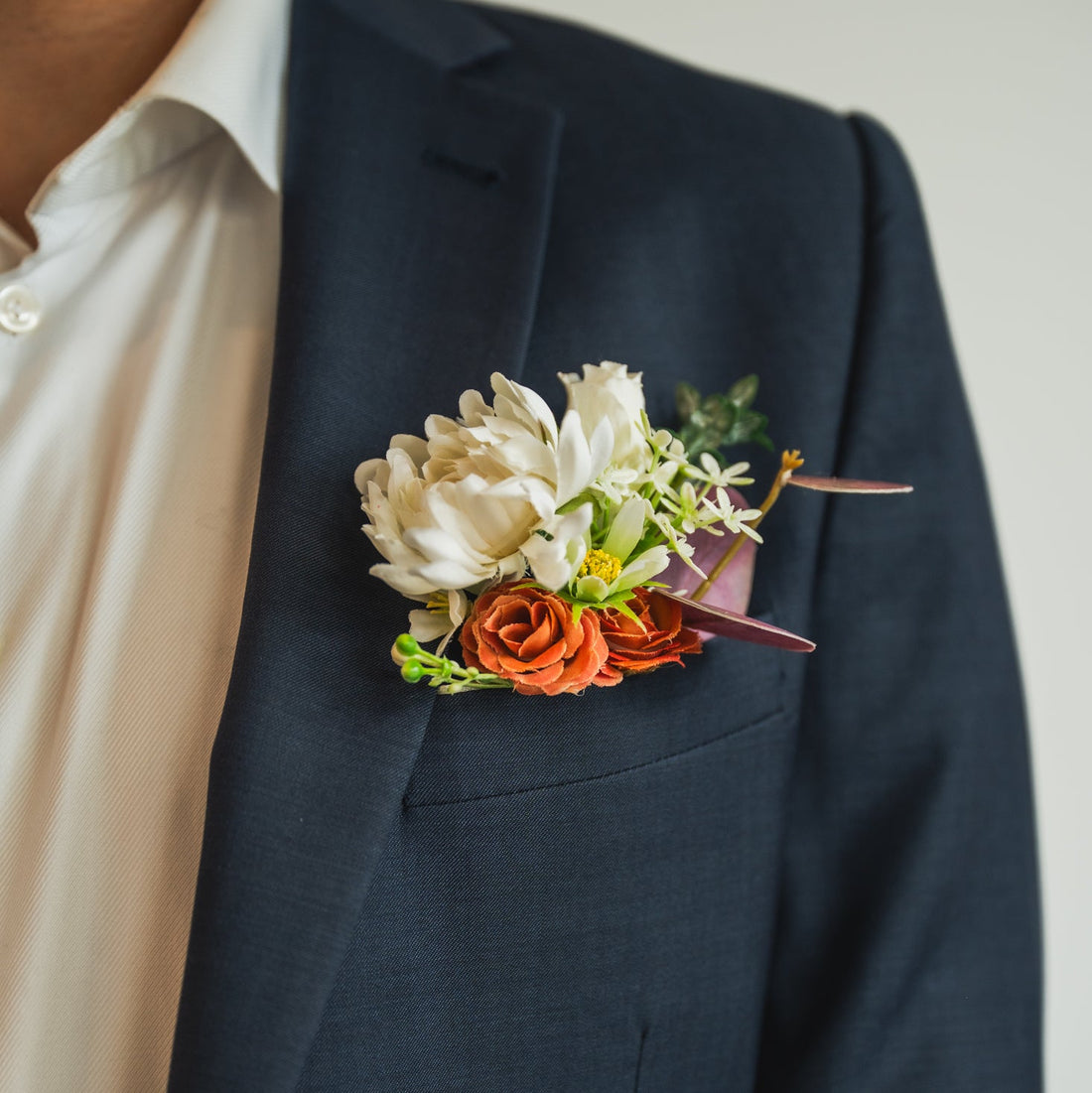 Cocoa Blooms groom’s boutonniere with faux terracotta rose, white flowers, and greenery on navy suit jacket – artificial wedding flowers rental in Edmonton.