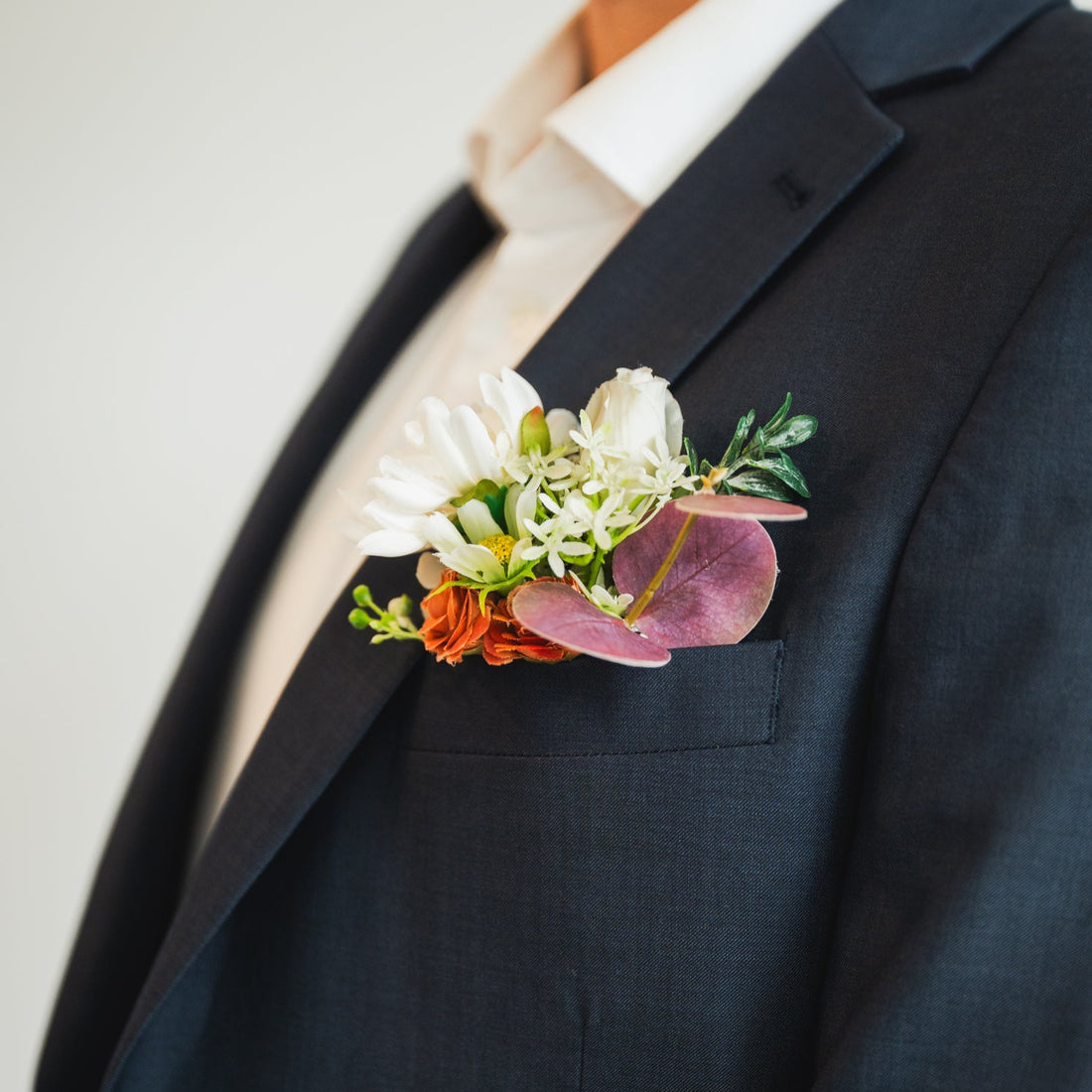 Close-up of Cocoa Blooms faux groom boutonniere with earthy terracotta and white blooms, accented with greenery – artificial boutonniere rental for weddings in Edmonton.
