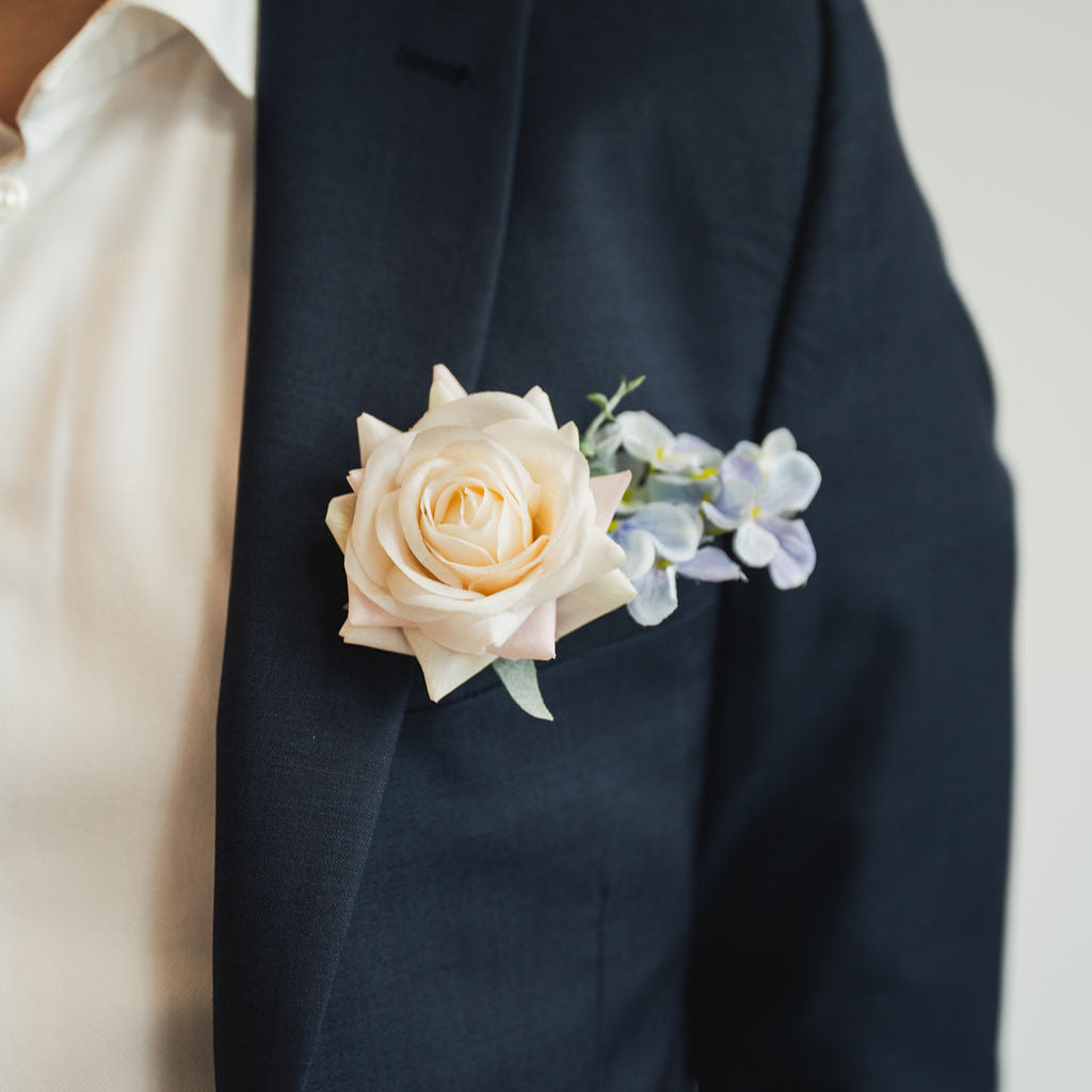 Navy suit jacket with a white rose boutonniere on a neutral background