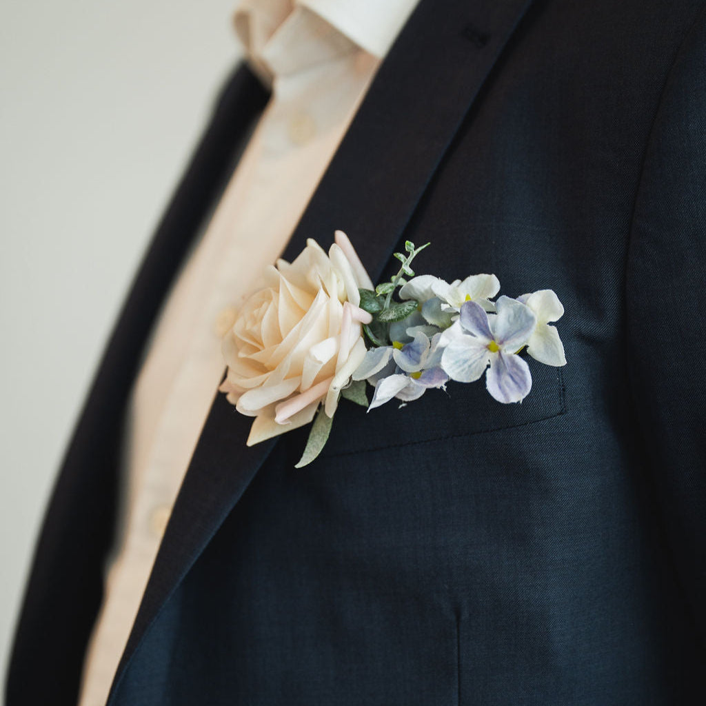 Close up of the Ocean Breeze groomsmen boutonniere which includes a milky pink, white rose and soft blue hydrangea and greenery.