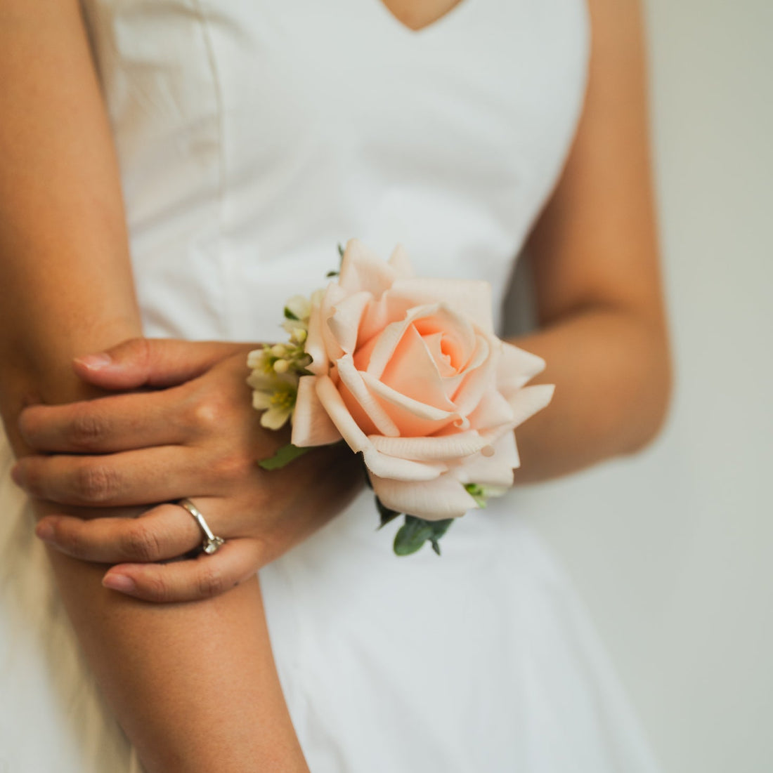 Pastel Petal faux corsage on model in white dress, artificial blush rose wrist flowers for Edmonton weddings and special events.