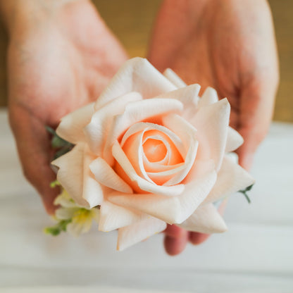 Hands holding artificial pastel rose corsage, real-touch faux flowers for Edmonton wedding corsage rentals.