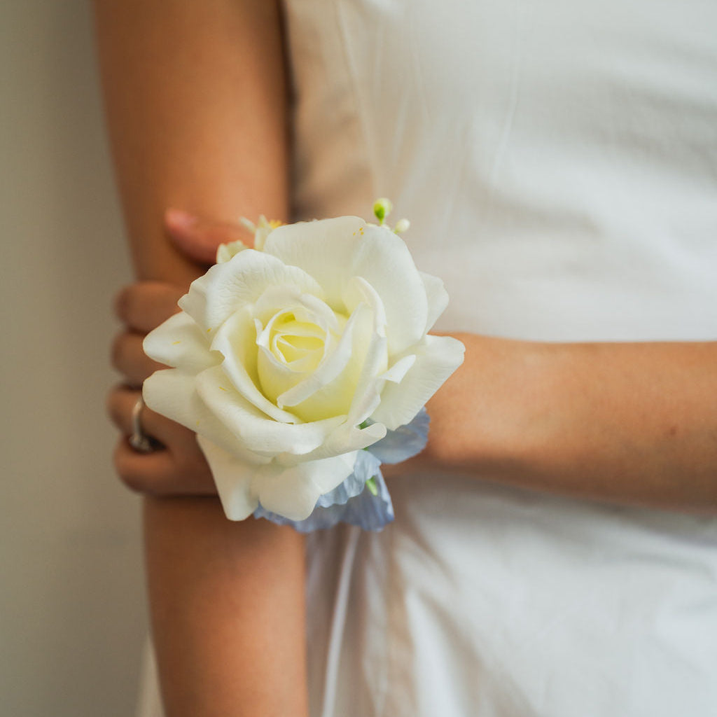 White rose corsage on a person wearing a white dress.