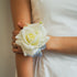 White rose corsage on a person wearing a white dress.