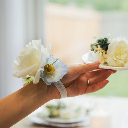 Hand reaching out wearing the Ocean Breeze corsage (faux white rose with blue cosmos)