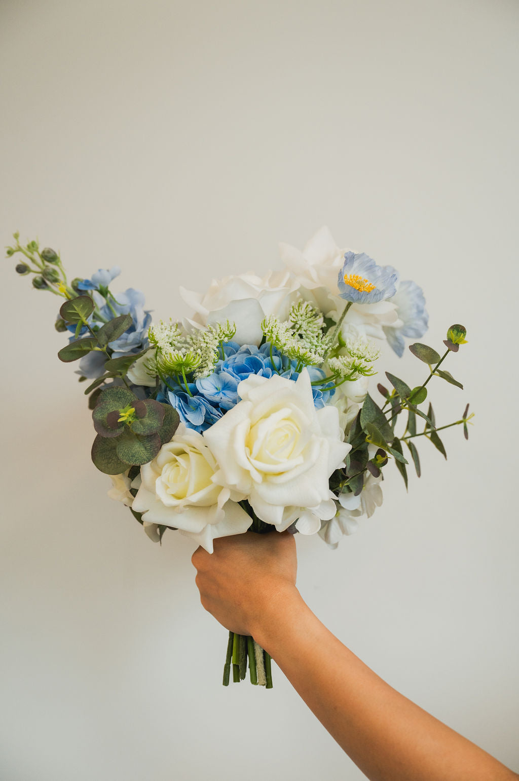 Faux flower bouquet of white and blue flowers held by a hand against a plain background