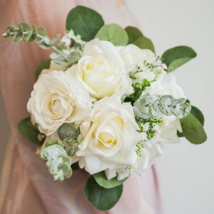 Bouquet of faux white roses with greenery held by a person against a neutral background