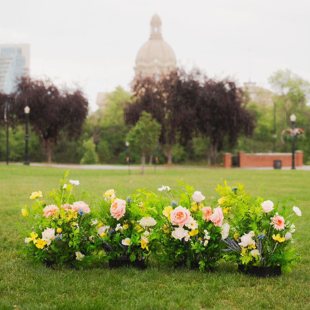 Wildest Dreams floor floral arrangements group in fours on grass with a blurred background near the Alberta Legislature building. 