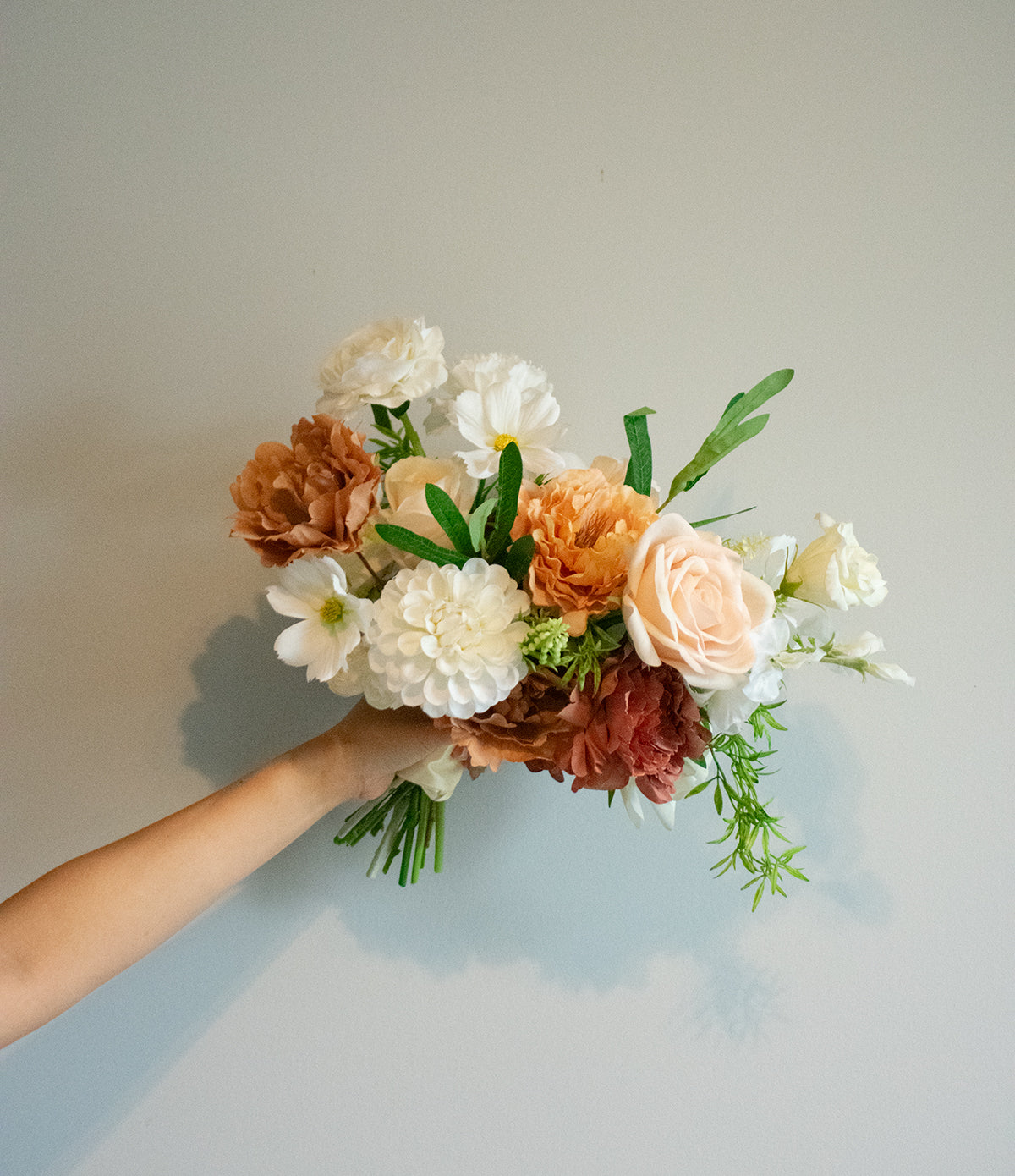 Bouquet of artificial flowers held by a person against a plain background
