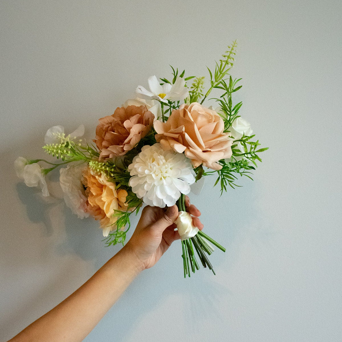 Bouquet of real touch and silk bridesmaid bouquet held by a hand against a plain background