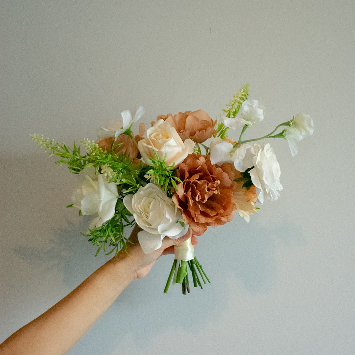 Bouquet of faux flowers held by a hand against a plain background