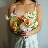Woman holding a bouquet of artificial/silk blush and coffee flowers against a neutral background
