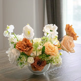 Faux floral centrepiece in a white vase on a wooden table with a blurred background
