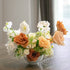 Faux floral centrepiece in a white vase on a wooden table with a blurred background