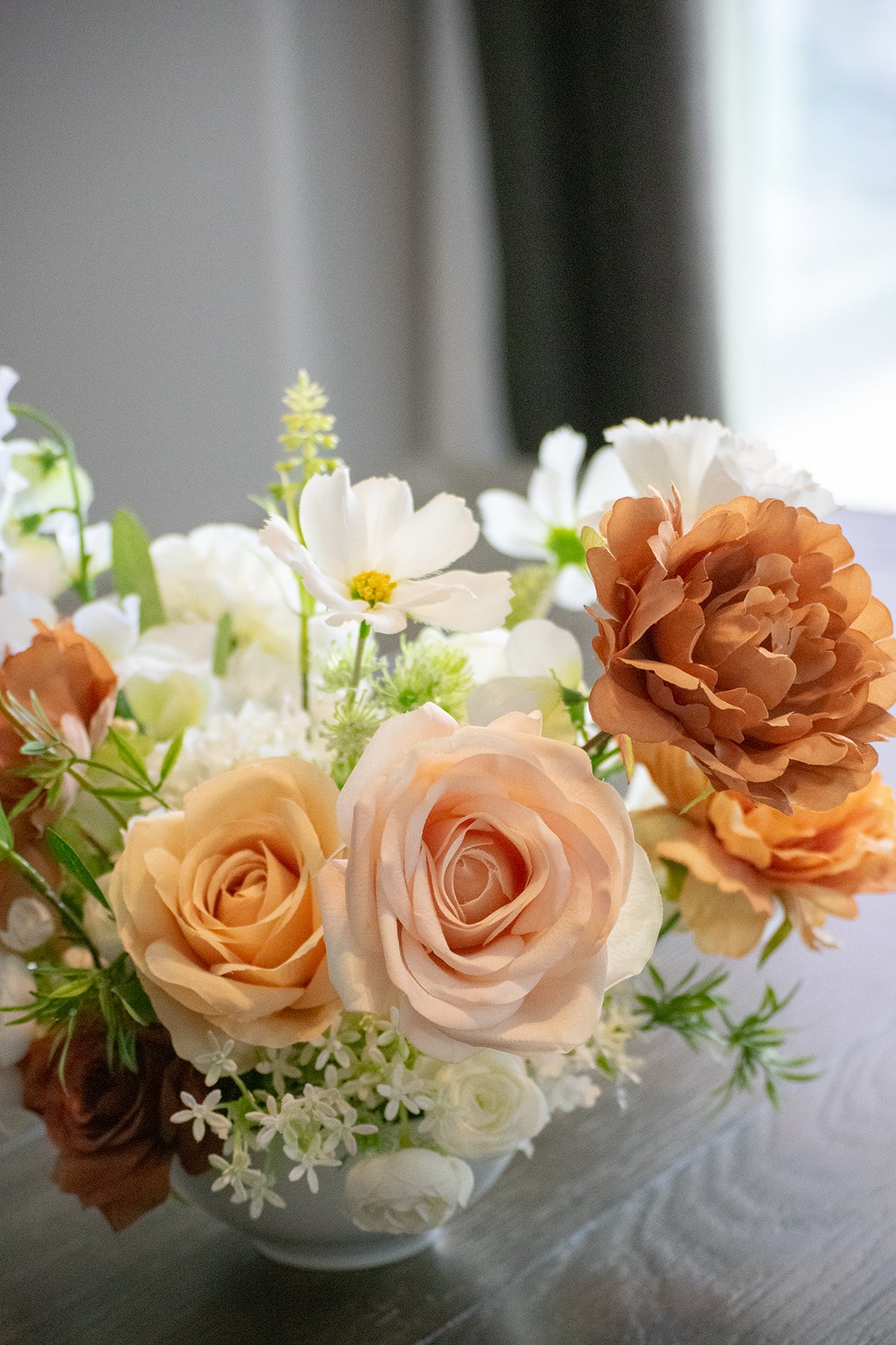 Close up of light brown, peach, blush and white faux flowers (silk and real touch) in a white vase on a reflective surface.