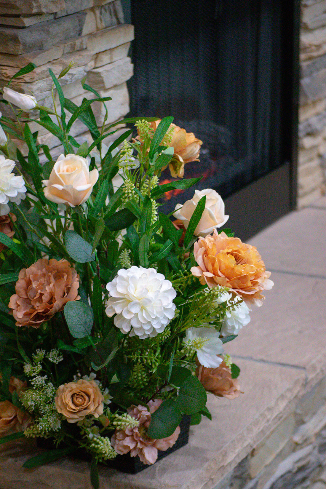 Floral silk and real touch arrangement with peach and white flowers in front of a stone fireplace.