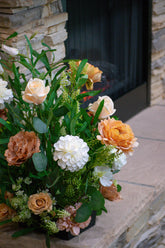 Floral silk and real touch arrangement with peach and white flowers in front of a stone fireplace.