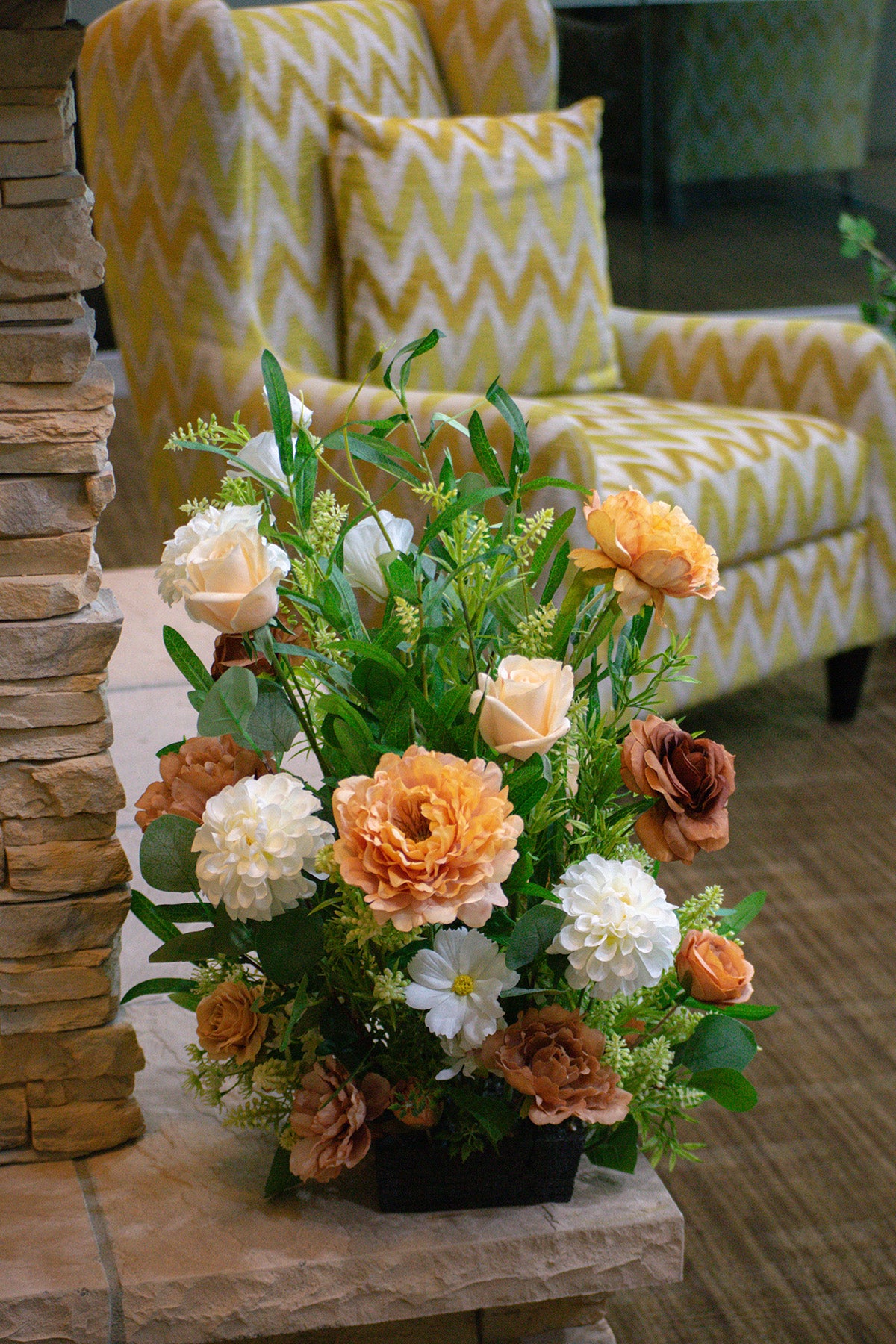 Floral arrangement on a stone surface with a yellow and white chevron-patterned chair in the background.